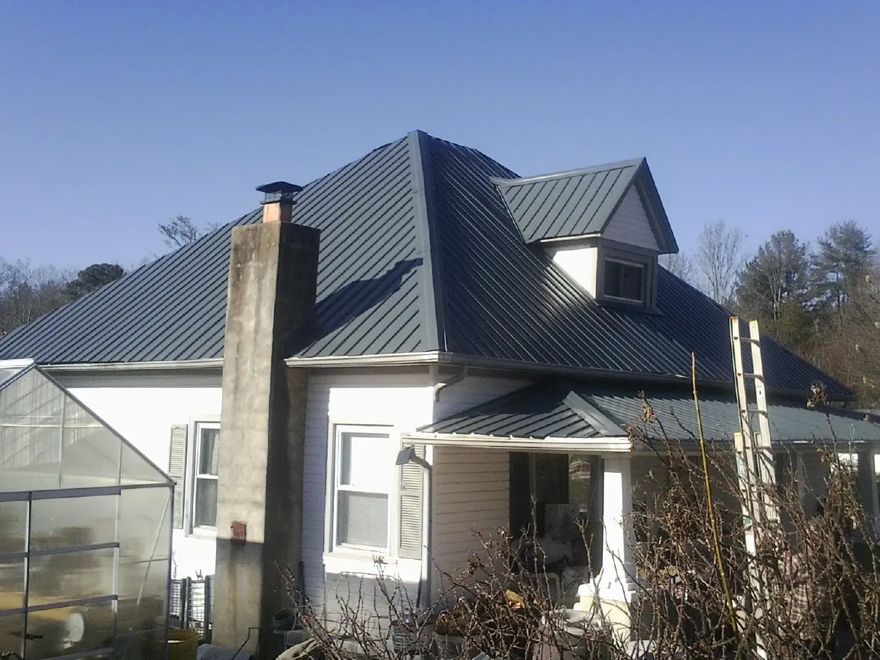 Dark blue standing seam metal roof on a white farmhouse with dormer — Slate & Tile Roof Repair by Roofing Brothers in Barnardsville