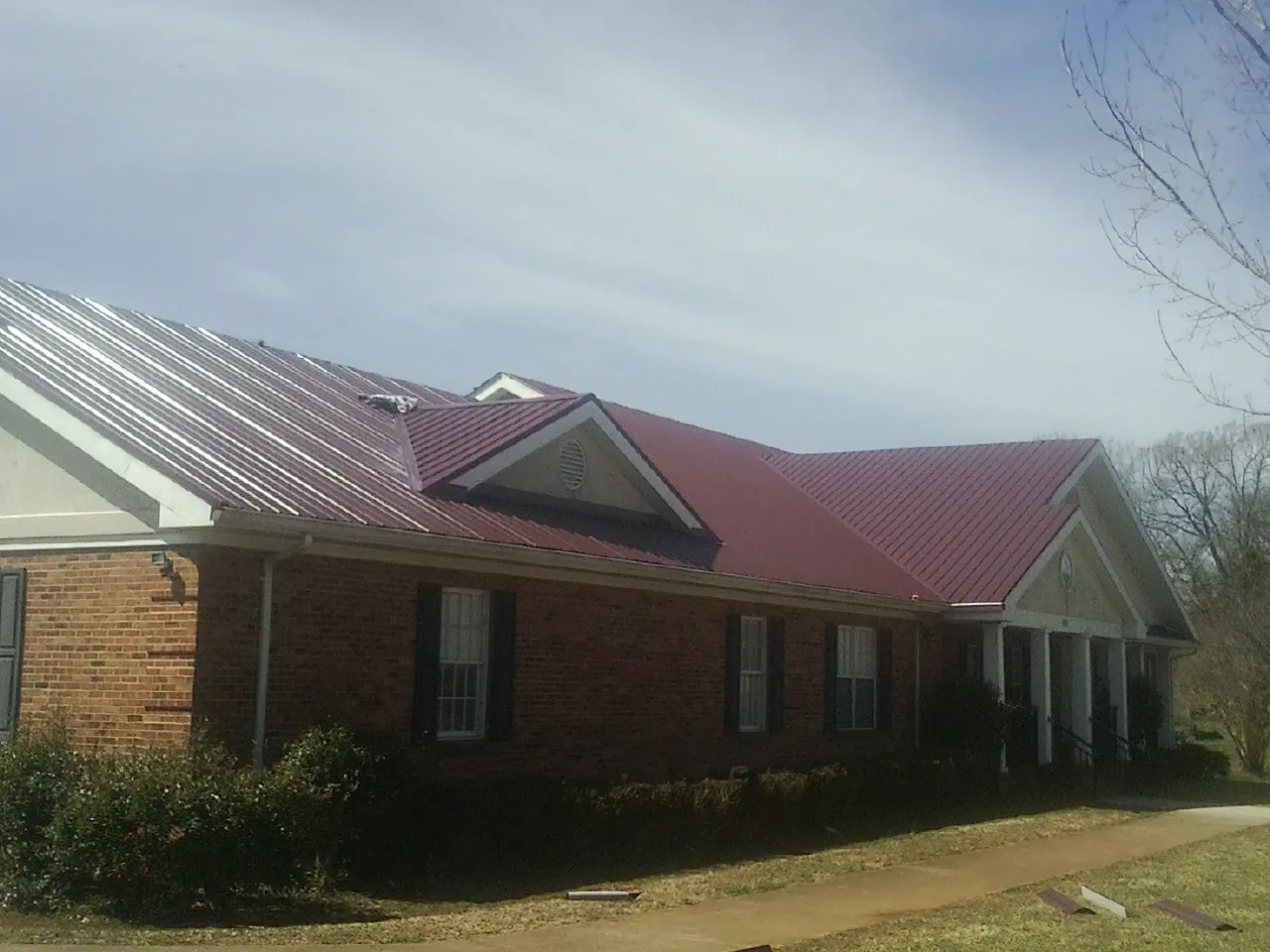 Red metal roof with gabled entries on a long brick building, from a Hail Damage Roof Repair job in Barnardsville