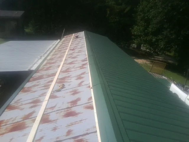 Old rusted panels beside newly installed green metal roofing — Wind Damage Roof Repair by Roofing Brothers in Barnardsville