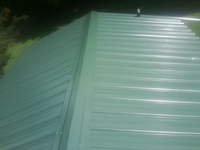 New green metal panels meeting at the ridge of a roof — Flat Roof Repair work by our crew in Barnardsville
