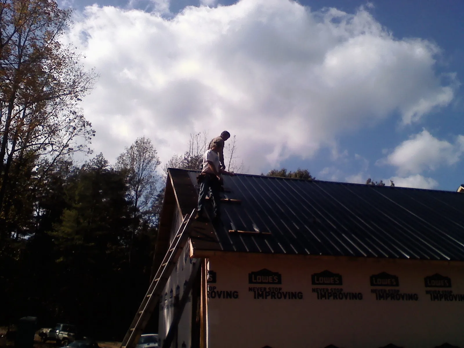 Roofer fastening dark metal panels high against a cloudy sky, from a Roof Inspection job in Barnardsville