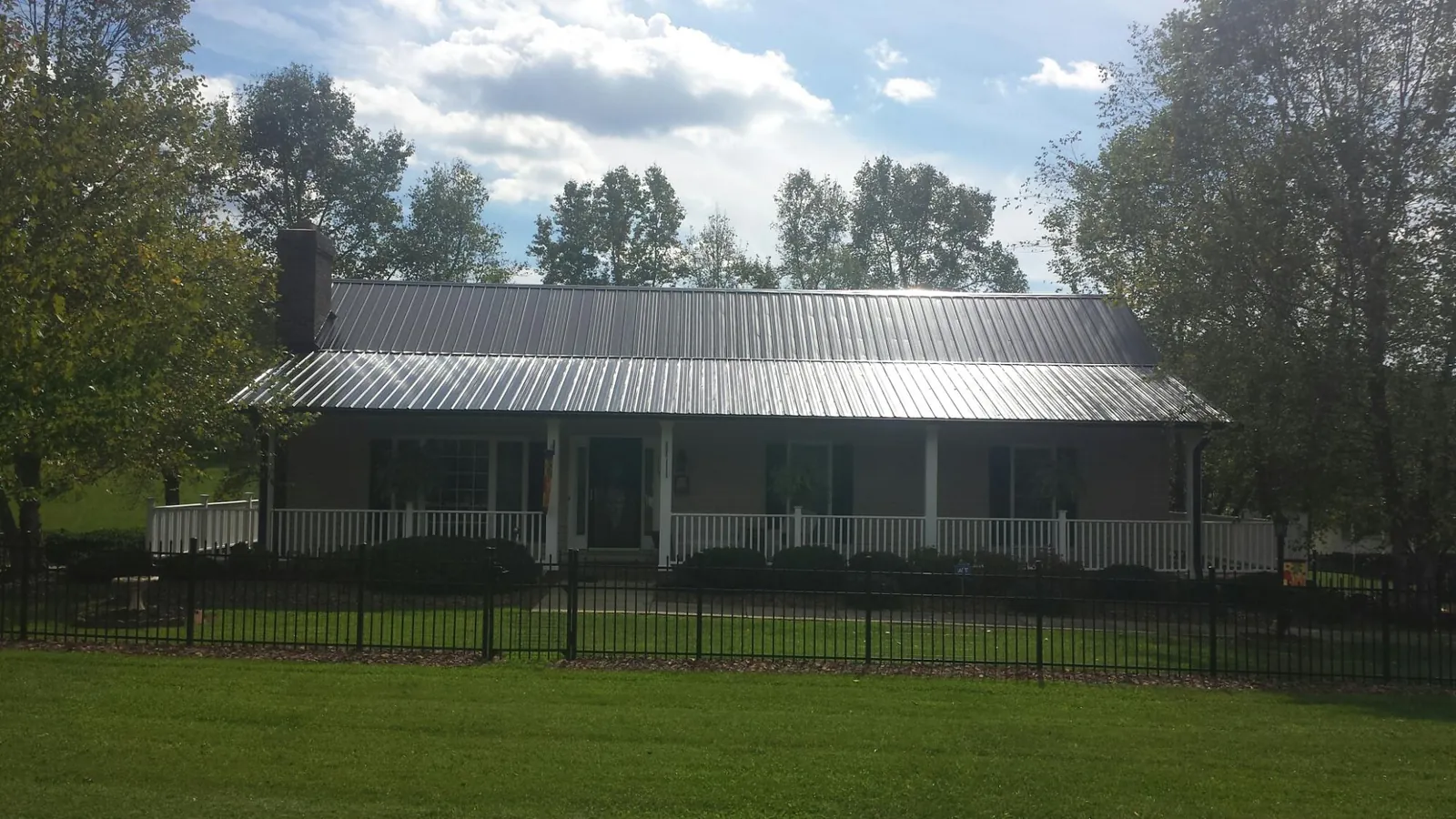 Gray metal roof on a brick ranch with a full width front porch — Gutter Guard Installation work by our crew in Barnardsville