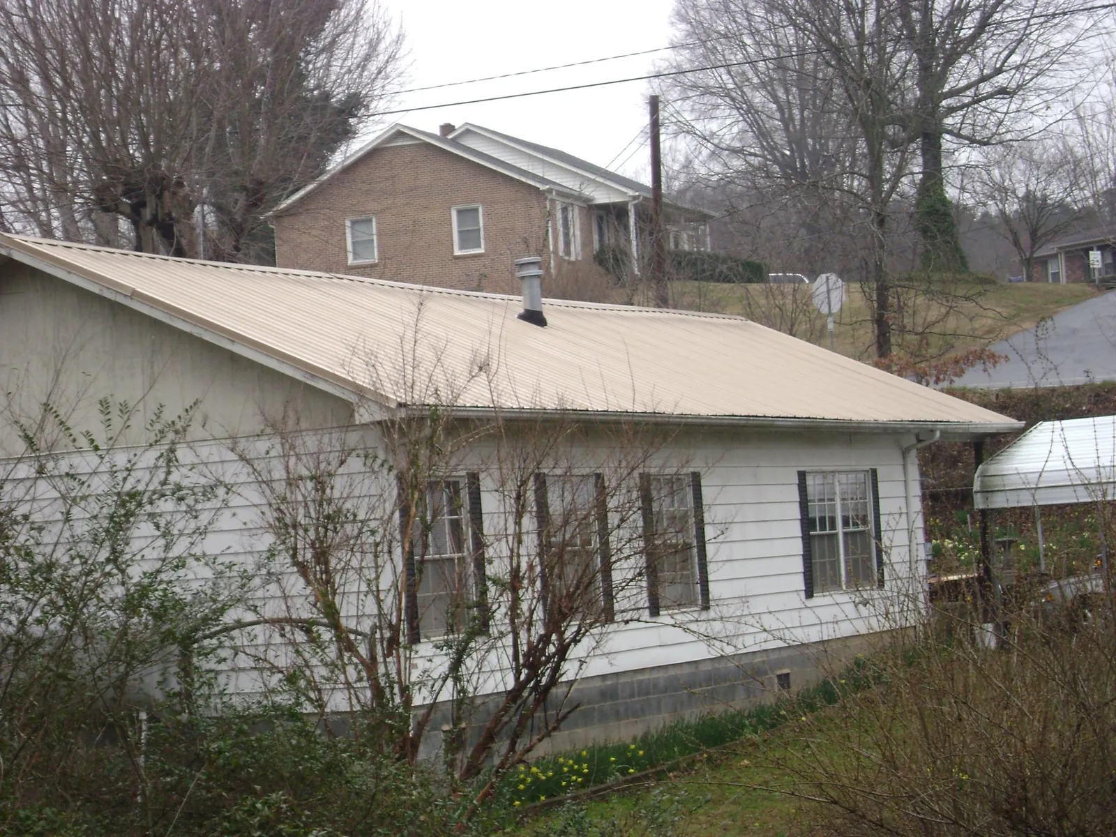 Tan metal roof on a white sided house set into a hillside — Commercial Roofing by Roofing Brothers in Barnardsville