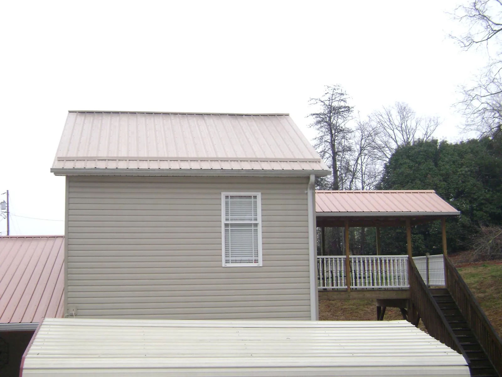 Tan metal roofs on a two story addition and attached porch, from a Roof Replacement job in Barnardsville